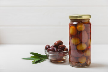 Olives in a glass jar on a white wooden background. pitted green olives in jar.Pickled olives in glass jar. On a wooden background.Marinaded olives. Space for text.Space for copy. Vegan food.
