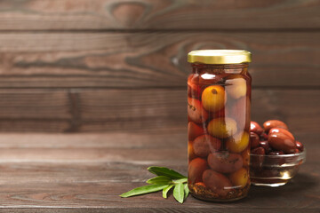 Olives in a glass jar on a brown wooden background. pitted green olives in jar.Pickled olives in...