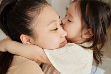 Asian little girl embracing and kissing her mom