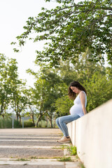 Naklejka premium Young pregnant woman looking her belly sitting in the street