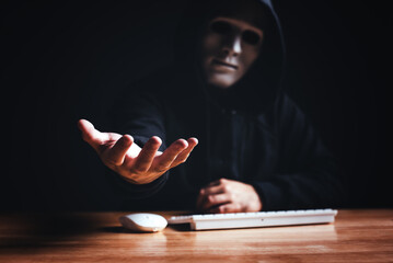 Black hood hacker force demands ransom by holding out his hand on table where sensitive data is...