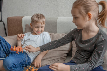 Little brother and sister play with plastic animals sitting on the couch. Love and friendship within the family, joint leisure and emotional interaction between children