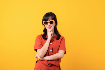 Portrait young beautiful asian woman happy smile dressed in orange clothes and sunglasses showing thinking gesture isolated on yellow studio background.