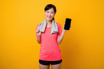 Naklejka premium Portrait young asian sports fitness woman happy smile wearing pink sportswear and smartphone doing exercise training workout against yellow studio background. technology wellness lifestyle concept.