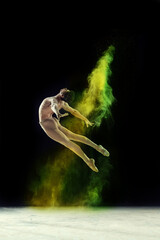 Obraz na płótnie Canvas Muscular young man, professional ballet dancer in motion, dancing with colorful powder explosion against black studio background. Concept of art, festival, beauty of dance, inspiration, youth