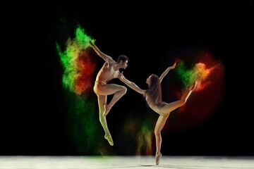 Beautiful young man and woman, talented ballet dancers in beige bodysuits dancing with colorful powder explosion against black background. Concept of art, festival, beauty of dance, inspiration, youth