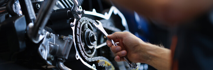 Male mechanic repairs amotorcycle motor with wrench in service center. Motorcycle maintenance and...