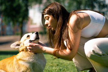 portrait of a young girl and a cute corgi dog, the owner kisses the dog on the nose on a walk in the park