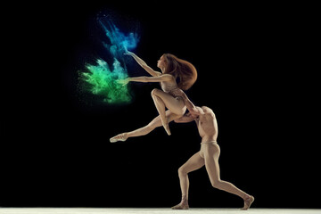 Fototapeta na wymiar Artistic young man and woman, talented ballet dancers in beige bodysuits dancing with colorful powder explosion against black background. Concept of art, festival, beauty of dance, inspiration, youth