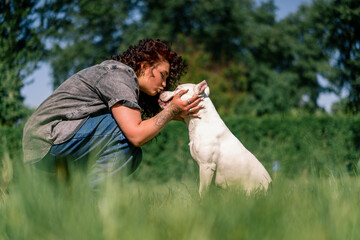 beautiful curly girl kisses the nose of a white dog of a large pit bull breed love for animals