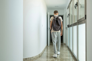Sad frustrated teenage boy walks away down school corridor alone. Education difficulties, problem...