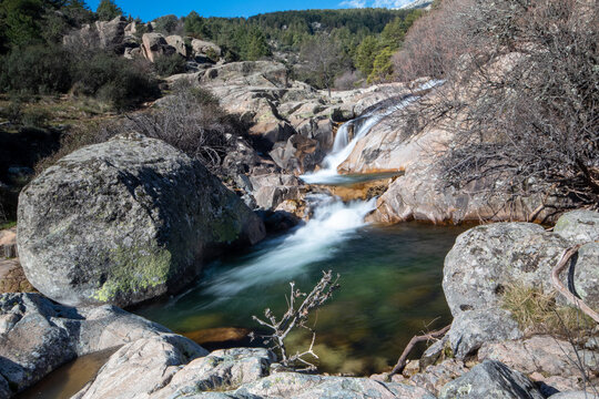 Una imagen que muestra una cascada en el río de La Pedriza. El agua cae en cascada desde lo alto de una formación rocosa, creando un hermoso efecto de movimiento y salpicaduras. 