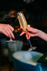 hands of two unknown women holding and clinking glasses cocktails in restaurant