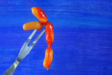 Tuinposter small sausages on vintage fork with dripping ketchup, free copy space, on blue background © Kirsten Hinte