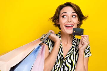 Fototapeta na wymiar Portrait of excited charming woman wear striped blouse look empty space hold card shopping bags isolated on yellow color background