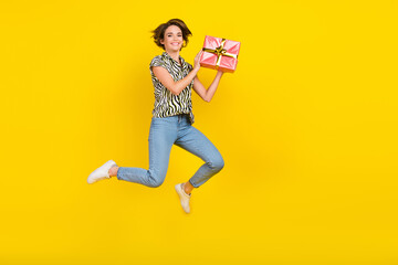 Full length photo of pretty sweet lady wear animal print shirt rising gift box jumping high isolated yellow color background