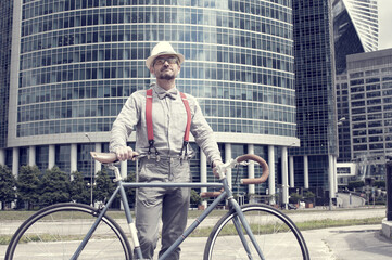 Adult hipster man with retro fixed gear bicycle on modern skyscrapers background. Vintage toned...