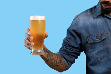 beer glass, male hand holds a glass with cold beer, foam on top of beer glass. on blue background