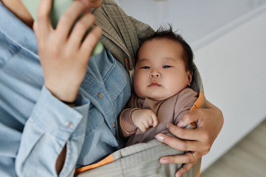 Close-up of mom holding her baby in sling while talking on mobile phone at home