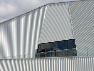 Minimalistic photo of an exterior of a modern tin building with a cloudy sky in the background	
