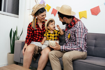 Brazilian Junina party at home. Family celebrating Festa Junina in the living room, wearing typical clothes and the wall decorated with colorful flags.