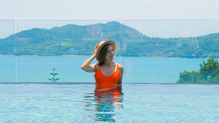 Woman in swimsuit and summer hat enjoys stunning sea view from infinity pool at luxury hotel spa. Relaxing and enjoying a peaceful vacation at this paradise resort.