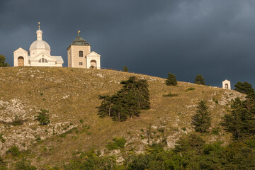 a hill with a chapel, lit by the setting sun and against a background of dramatic dark clouds just before the rain