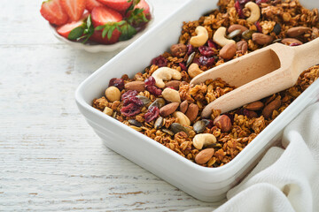 Homemade granola with greek yogurt or milk and cashews, almonds, pumpkin with dried cranberry seeds in old bowl on white rustic wooden table background. Healthy energy breakfast or snack. Top view.