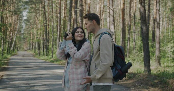 Man and woman standing in forest taking pictures with photo camera and talking enjoying vacation in summer. Photography and travelling concept.