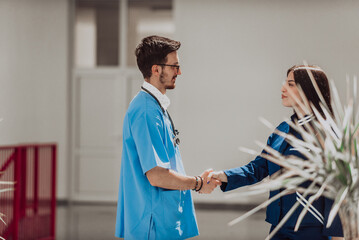 A doctor and the chief nurse of the medical department exchange a handshake in the hallway of a modern hospital, symbolizing their collaborative and respectful relationship in providing high-quality