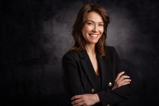 Studio portrait of a brunette haired mid aged woman sitting at isolated dark background