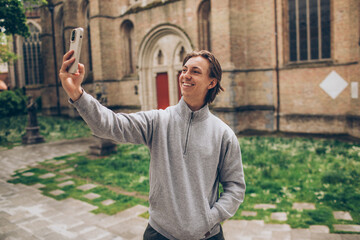 young man male teen adult tourist taking a cellphone iphone selfie in front of an old building in...