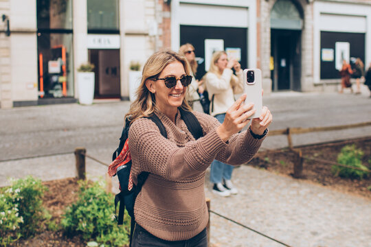 woman tourist wearing a backpack and a red bandana and sunglasses stops to take a photo with her iphone with other tourists behind her