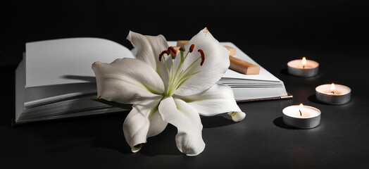 Lily flower with candles and book on dark background. Funeral concept