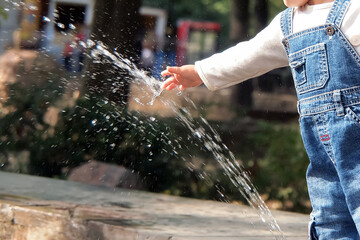 A child stretches out his hand into the jet of the city fountain.