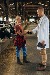 Veterinarian and female farmer shaking hands in cow stable
