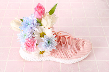 Obraz na płótnie Canvas Sneaker with spring flowers on pink tile background