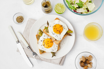 Delicious sandwiches with fried eggs and asparagus on light background