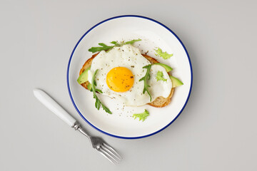 Delicious sandwich with fried egg, avocado and arugula on grey background