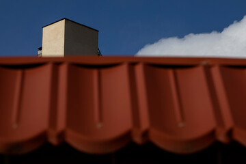 A composite image of blue sky, roof, clouds and part of a modern building