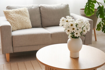 Vase with chrysanthemum flowers on wooden coffee table in living room