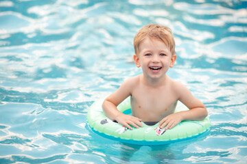 Fototapeta na wymiar happy child bathes in water. Swimming lessons, summer vacation. cute little boy smiling, having fun in the pool in the swimming circle. safety of children near the water. family vacation concept