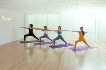 Naklejka premium Four women doing the warrior pose inside a studio while taking their yoga class
