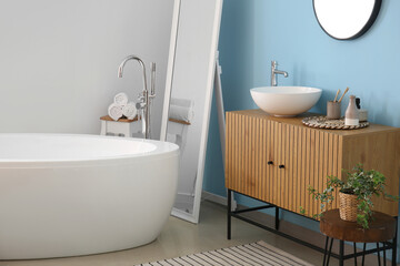 Fototapeta na wymiar Interior of stylish bathroom with wooden cabinet, bathtub, mirror and sink