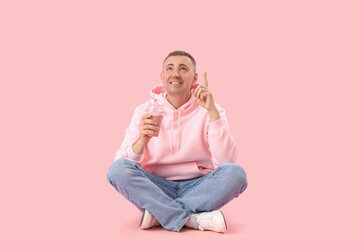 Obraz na płótnie Canvas Mature man with glass of fruit smoothie pointing at something on pink background