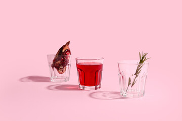 Glasses of fresh pomegranate juice and rosemary on pink background