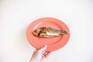 A whole fried carp with a fried crust, served on a bright red plate. A hand holds a plate on a white background.