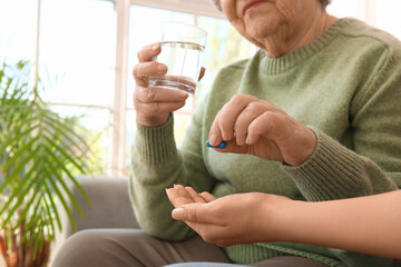 Young woman giving pills to her grandmother at home, closeup