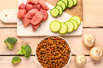 Composition with dry pet food, raw meat and natural products on light wooden background