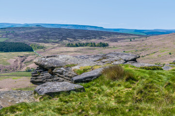 A view past millstone rock slabs towards the valley below from the Stanage Edge escarpment in the Peak District, UK in summertime